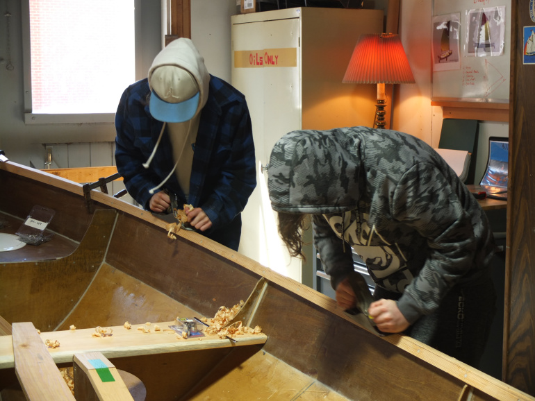 Students using hand tools to build a boat in the boat shed at the Maritime Museum of the Atlantic.