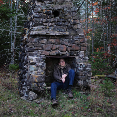 Steve Skafte sitting in a stone fireplace in the woods.