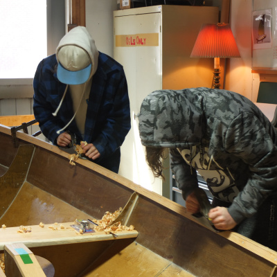 Students using hand tools to build a boat in the boat shed at the Maritime Museum of the Atlantic.