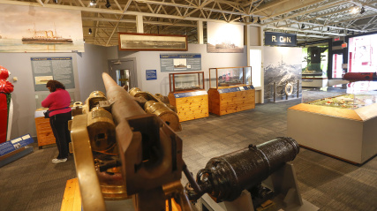 Visitors exploring the Navy Gallery, cannon in the foreground.
